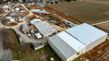 Çok sayıda bina ve devam eden faaliyetlerle, kırsal bir alanda yoğun bir inşaat sahası görülüyor. İşçiler görülebilir ve inşaat makineleri mevcut, bu da ilerlemeyi gösteriyor.