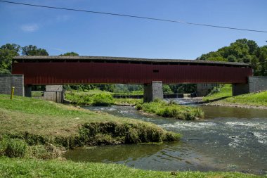 Berrak bir mavi gökyüzünün altında yemyeşil ve ağaçlarla çevrili sakin bir nehrin üzerinden tarihi bir köprü geçer. Barışçıl ortam, doğaya ve mimariye bir bakış sunuyor..