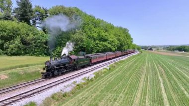 Ronks, Pennsylvania, 18 Mayıs 2023 - Buharlı lokomotif yemyeşil ve açık alanlı piknik alanına çekilir ve nostaljik seyahat deneyimi göz kamaştırıcı renkler sunar.