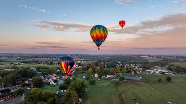 Üç canlı sıcak hava balonu, çiftlik ve evlerle dolu huzurlu bir arazinin üzerinde zarifçe süzülür..
