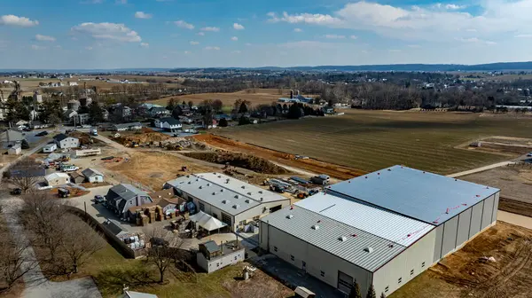 Gelişmekte olan bir kırsal alanda, küçük evler ve tarım arazilerinin yanında büyük bir depo inşa ediliyor..