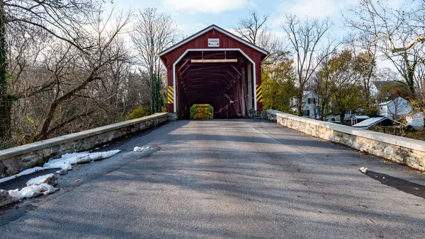 Güneşli bir öğleden sonra, ağaçların ve banliyö evlerinin arasında huzurlu bir şekilde uzanan büyüleyici bir köprü. Yapıda klasik tasarım sergilenmektedir ve çıplak dallar ve kar kalıntıları tarafından çevrelenmiştir..