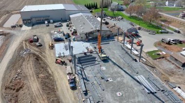 Ağır makineler aktif olarak yeni bir bina inşa ediyor. Turnalar çelik kirişleri kaldırırken, işçiler açık bir günde işleme nezaret ediyorlar..