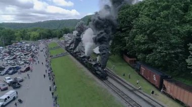 Cass, Batı Virginia, 18 Haziran 2022 - Pürüzsüz dinamik hareketin keyfini çıkaran kalabalıkla manzaralı yeşil bir manzarada duman yayan buhar trenlerinin hava görüntüleri zengin detay