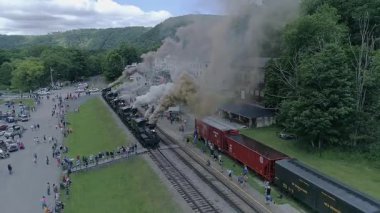 Cass, Batı Virginia, 18 Haziran 2022 - Buhar trenleri, ziyaretçiler rayların yakınındaki bir sergi için toplanırken duman bulutları salıyor. Hevesler ve aileler tarihi motorları keşfediyor..