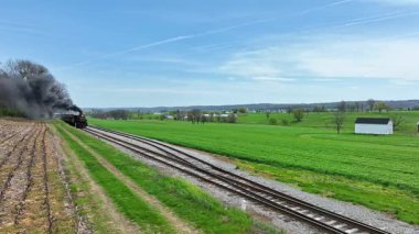 Tarihi bir buhar treni, canlı yeşil alanlarda süzülürken kalın siyah dumanlar püskürtür. Bu huzurlu yolculuk, ilkbaharda kırsal manzaraların güzelliğini gözler önüne seriyor..