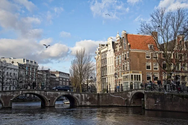 アムステルダム オランダ 2014年12月31日 人々はオランダのアムステルダムで冬の日差しの中で飛んでいるカモメと運河を渡って橋の上を歩く — ストック写真