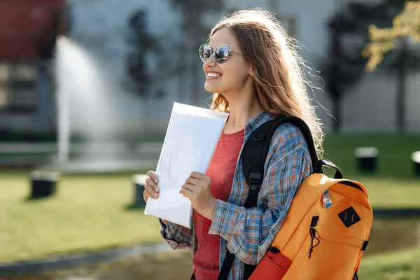 在大学里 年轻的金发嬉皮士女学生背着背包在户外微笑 图库照片