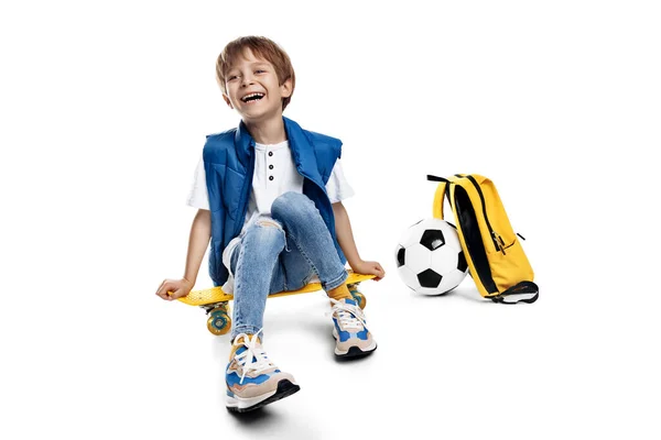 可爱的金发男孩坐在白色背景的黄色滑板上 回学校去 — 图库照片