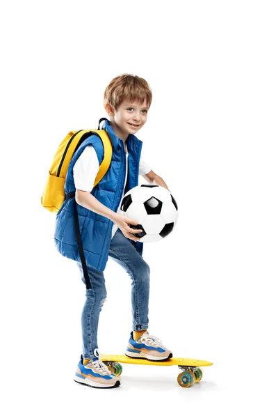 聪明的小男孩 带着滑板和背包 拿着白色背景的足球 回学校去 免版税图库图片