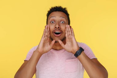 Başarılı Afrikalı Amerikalı genç adam. Elleri ağzının önünde, sarı arka planda.