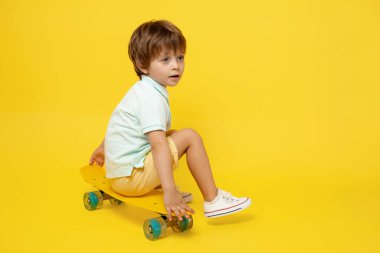 Yazlık kıyafetli, pennyboard ya da kaykaylı sarı arka planda küçük sevimli bir çocuk.