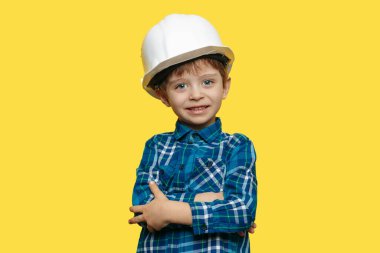 Küçük çocuk mühendis ya da mimar, sarı arka planda koruyucu miğfer takıyor.