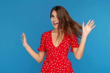 Mavi arka plan üzerinde mutlu duygu kırmızı elbise parlak gülümseme ile güzel genç kadın