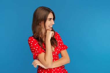 Mavi arka plan üzerinden uzağa bakan kırmızı elbiseli parlak bir gülümseme ile heyecanlı genç kadın