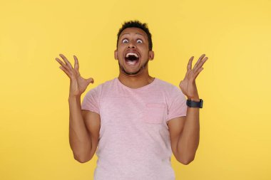 Sarı arka planda elleri havada, bağıran Afrikalı Amerikalı genç adam. Komik Yüz İfadesi