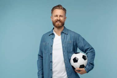 Neşeli sakallı sarışın hippi klasik futbol topuyla stüdyoda poz veriyor.