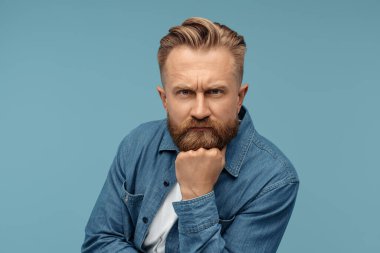 Mavi arka planda kot gömlekli ciddi sakallı hippi sarışın adam. Adam şüpheli görünüyor..