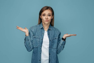 Mavi arka planda, yüzünde şüpheli bir ifade olan güzel bir genç kadın.