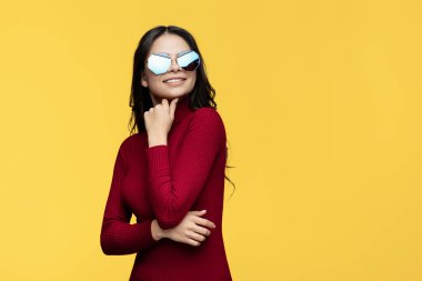 Kırmızı elbiseli ve güneş gözlüklü şık genç bayan sarı arka planda el üstünde poz veriyor. Uzaklara bakıyorum..