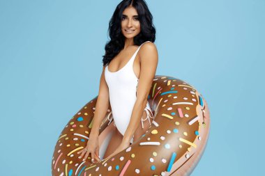 Mayo giymiş, mavi arka planda donut şişirilebilir daire şeklinde poz veren neşeli zinde genç bir kadın.