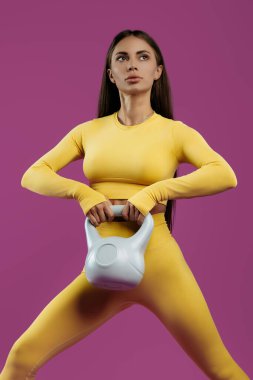 Mor arka planda gri kettlebell ile fonksiyonel egzersizler yapan zinde genç esmer kadın..