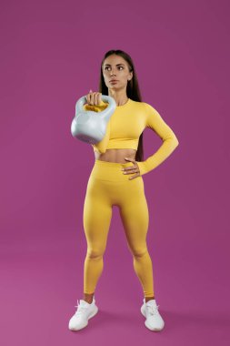Sportif genç esmer kadın, mor arka plan üzerinde gri kettlebell ile egzersiz yapıyor.