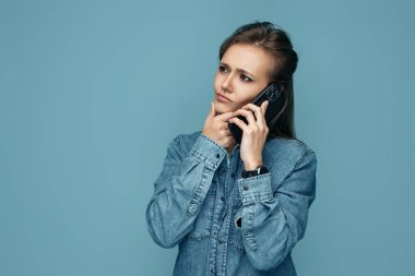 Genç bir kadının mavi arka planda akıllı telefondan konuştuğunu düşünüyorum.
