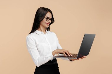 Bej arka planda, dizüstü bilgisayarda çalışan, olumlu, genç, modern iş kadını..