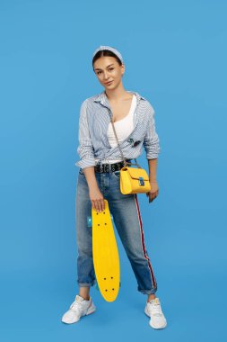 Sarı kuruşlu ya da kaykaylı modaya uygun genç bir kadın mavi arka planda poz veriyor..