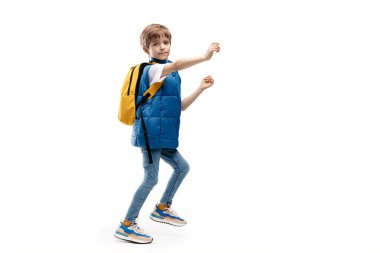 Sırt çantalı beyaz arka planda yürüyen küçük bir çocuğun tam boy görüntüsü. Okula geri dön. Kameraya bakıyorum..