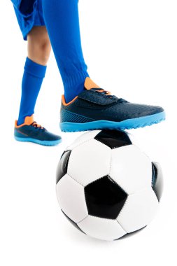 Yakın plan görüntü, genç futbolcu, mavi spor kıyafetli beyaz arka planda klasik futbol topunun bacağını tutuyor..