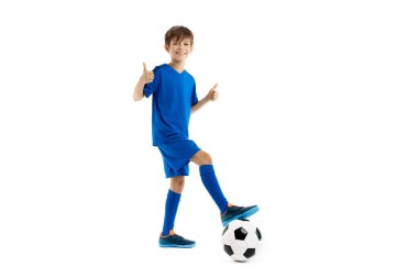Genç futbolcu, mavi spor kıyafetli klasik futbol topunun bacağını tutuyor ve beyaz arka planda baş parmak gösteriyor..