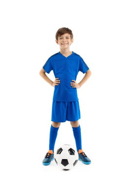 Mavi spor kıyafetli, beyaz arka planda klasik futbol topuyla poz veren kendinden emin genç bir çocuk..