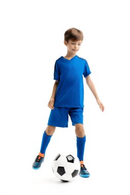 Beyaz arka planda klasik futbol topuyla oynayan mavi spor kıyafetli yakışıklı bir çocuk. Spor ve motivasyon.