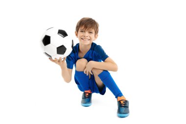 Mavi spor kıyafetli sevimli genç beyaz arka planda klasik futbol topuyla poz veriyor..