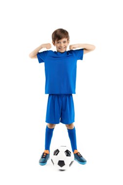 Mavi spor kıyafetli, beyaz arka planda klasik futbol topuyla poz veren kendinden emin genç bir çocuk. Uzaklara bakıyorum..