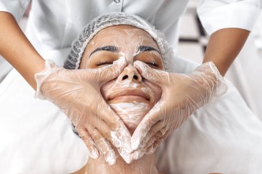 Kozmetolog kozmetoloji salonunda kadın yüzüne krem sürüyor.