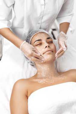 Kozmetolog kozmetoloji salonunda kadın yüzüne krem sürüyor.