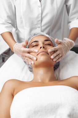 Kozmetolog kozmetoloji salonunda kadın yüzüne krem sürüyor.