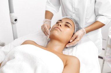 Kozmetolog kozmetoloji salonunda kadın yüzüne krem sürüyor.