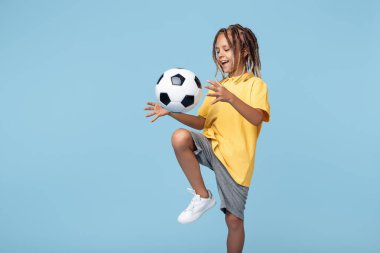 Afrika korkusu olan mutlu küçük çocuk mavi arka planda futbol topu atıyor.