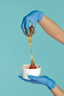 Mavi arkaplan üzerinde tüy dökme işlemi için şekerli kovayı tutan eller