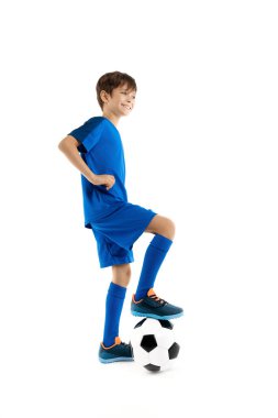 Sevimli genç futbolcu, mavi spor kıyafetli klasik futbol topunun bacağını tutuyor..