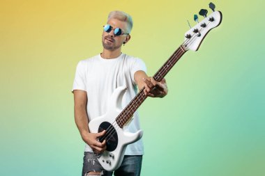 Yakışıklı hippi, renkli arka planda beyaz bas gitar çalıyor. Rock müzik konsepti.