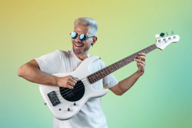 Havalı hippi adam renkli arka planda beyaz bas gitar çalıyor. Rock müzik konsepti.