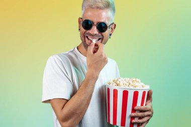 Çekici hipster adam elinde patlamış mısırla renkli bir arka plan tutuyor.