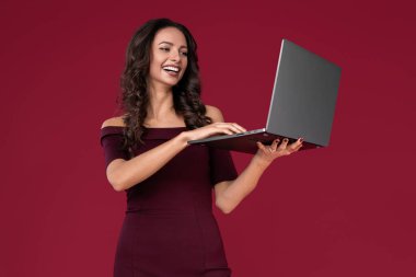 Kestane rengi elbise giymiş güzel genç bir kadın kırmızı arka planda bilgisayar ya da defter üzerinde parmak işareti yapıyor..