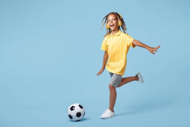 Afrika korkusu olan mutlu küçük çocuk mavi arka planda futbol topu atıyor.