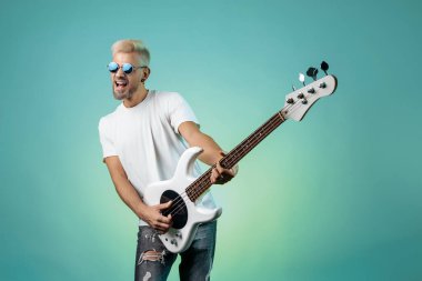 Hippi adam renkli arka planda beyaz bas gitar çalar. Rock müzik konsepti.